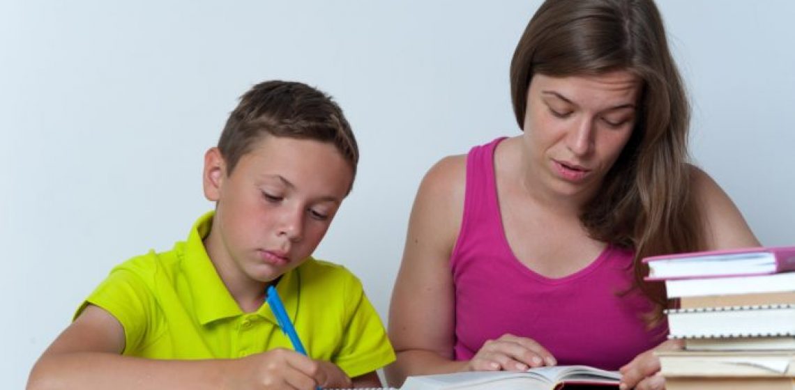 Caucasian mother and school child sitting together, doing homework lessons at home. Happy family relations. Education concept.